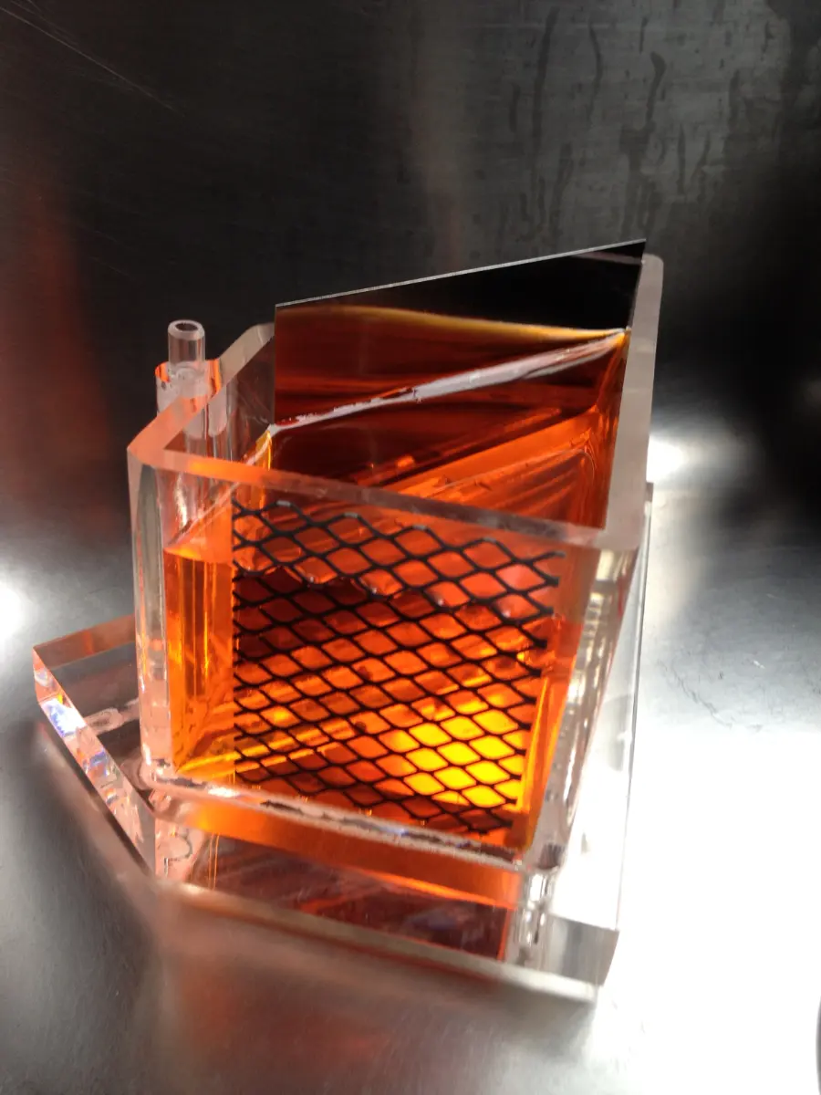 Transparent laboratory vessel containing an orange liquid, metal plates and a mesh panel